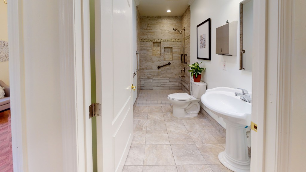 A modern bathroom with tiled flooring, featuring a shower, toilet, and sink.