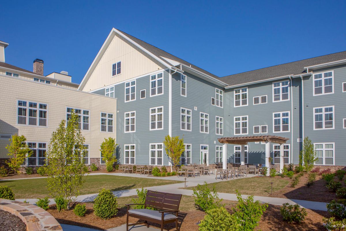 A modern residential building with a landscaped garden and benches in the foreground.