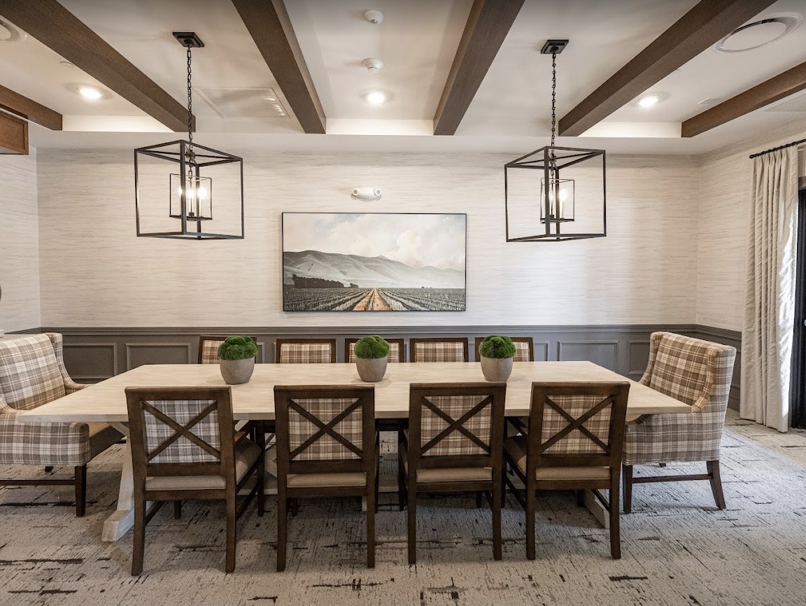 A stylish dining room featuring a wooden table surrounded by chairs, accented with hanging lights and ceiling beams, complemented by wall art and small plants.