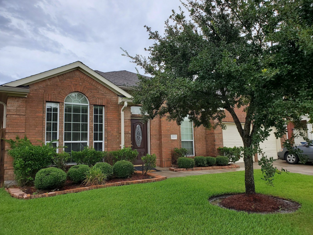 A suburban brick house with a well-maintained front yard and tree.