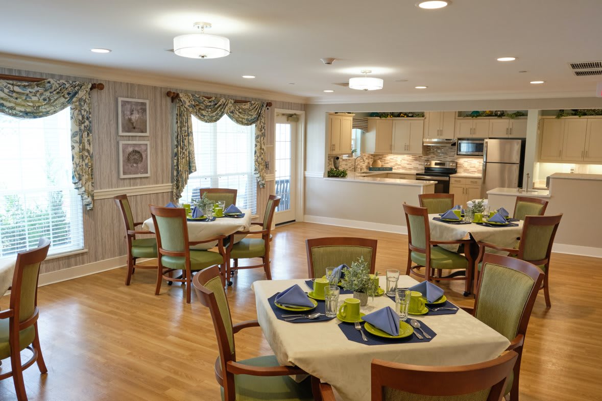 Elegant dining room with neatly arranged tables and chairs, featuring a view into an open kitchen area.
