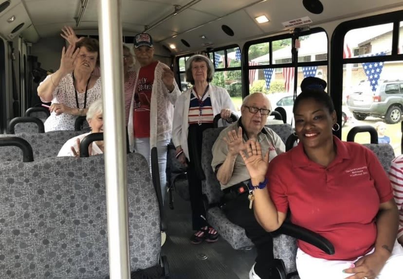 A group of people smiling and waving while seated inside a bus.