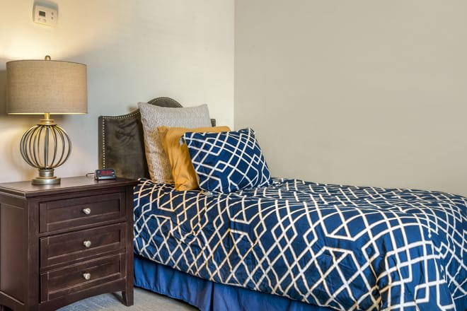 A neatly made bed with geometric-patterned bedding and several decorative pillows beside a wooden nightstand with a lamp.