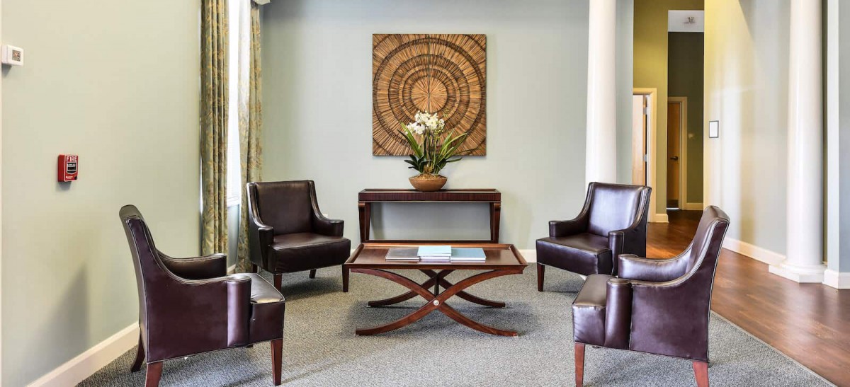 A cozy waiting room with four leather chairs, a wooden coffee table, and decorative wall art.