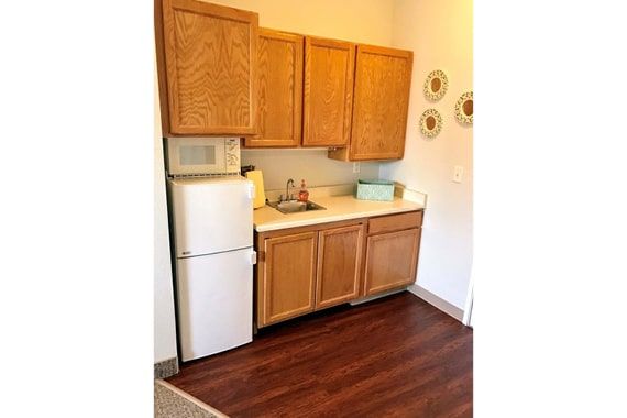 A compact kitchen area with wooden cabinets, a small refrigerator, microwave, and a sink on a countertop.