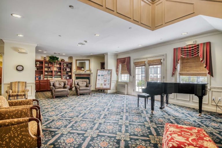 A spacious living room features a grand piano, armchairs, and bookcases.