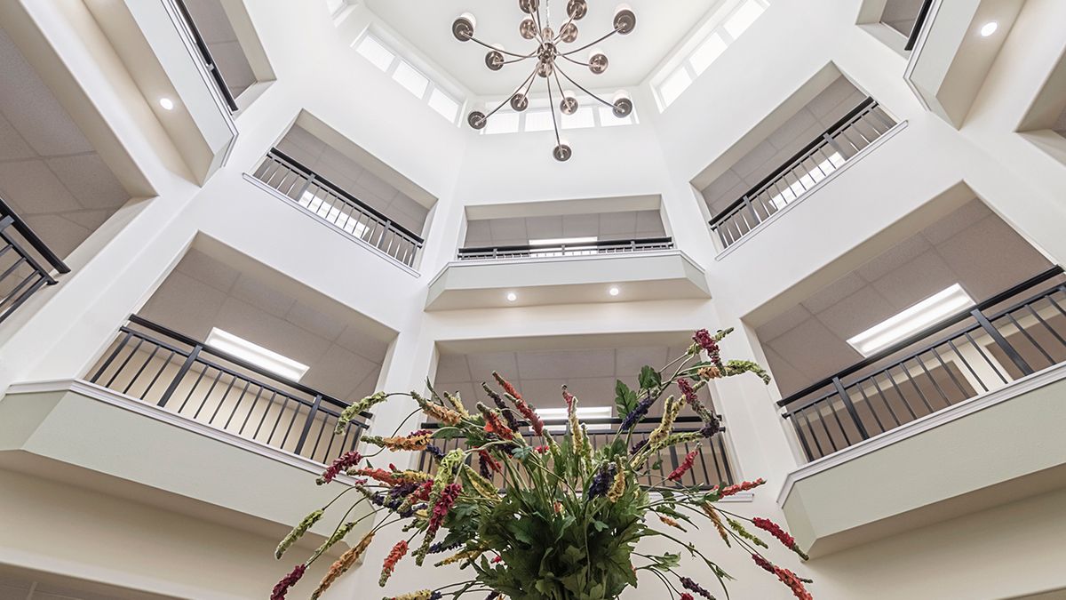 A modern atrium with multiple balconies, featuring a central chandelier and decorative plants.