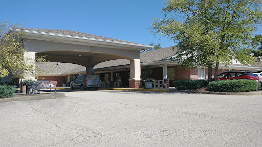 A view of a commercial building with a covered entrance and parked vehicles on a sunny day.