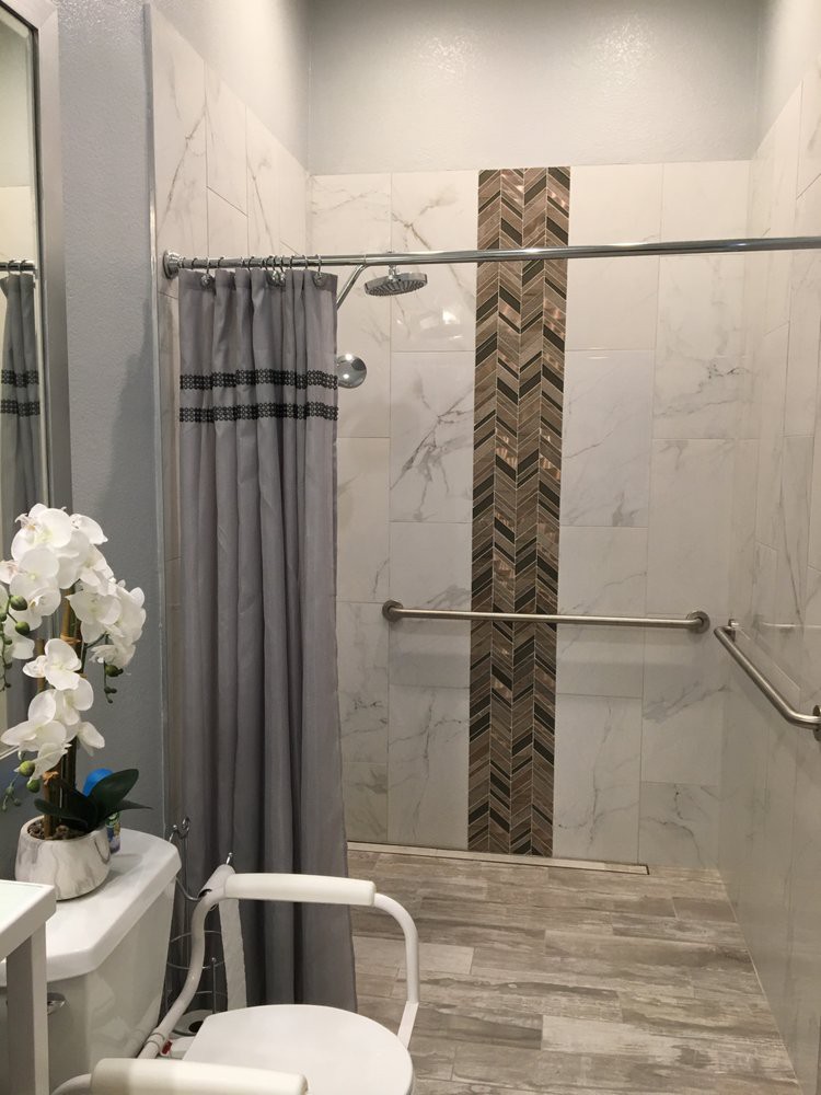 A modern bathroom with a stylish tile design in the shower, featuring a grab bar and decorative flowers.