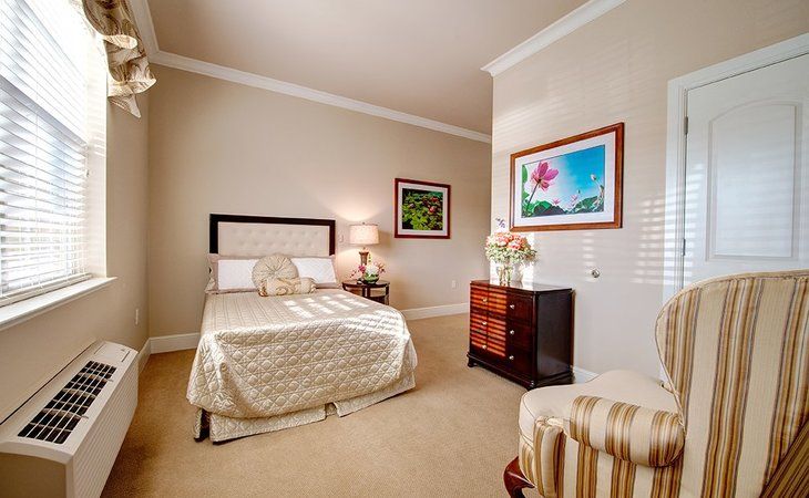A cozy and elegantly decorated bedroom featuring a bed, side table with a lamp, artwork on the walls, and patterned textiles.