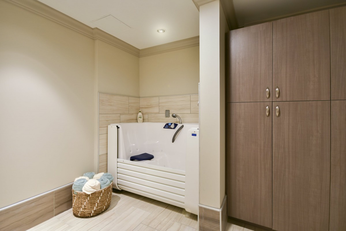 A modern bathroom with an accessible bathtub, storage cabinet, and a basket of towels.