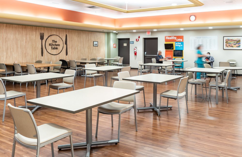 A modern cafeteria with empty tables and chairs on a wooden floor.