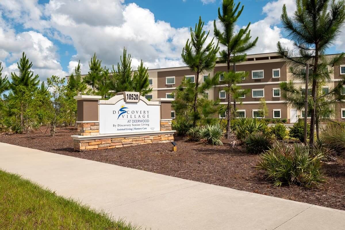 A modern building with a landscaped exterior and a prominent sign under a cloudy blue sky.