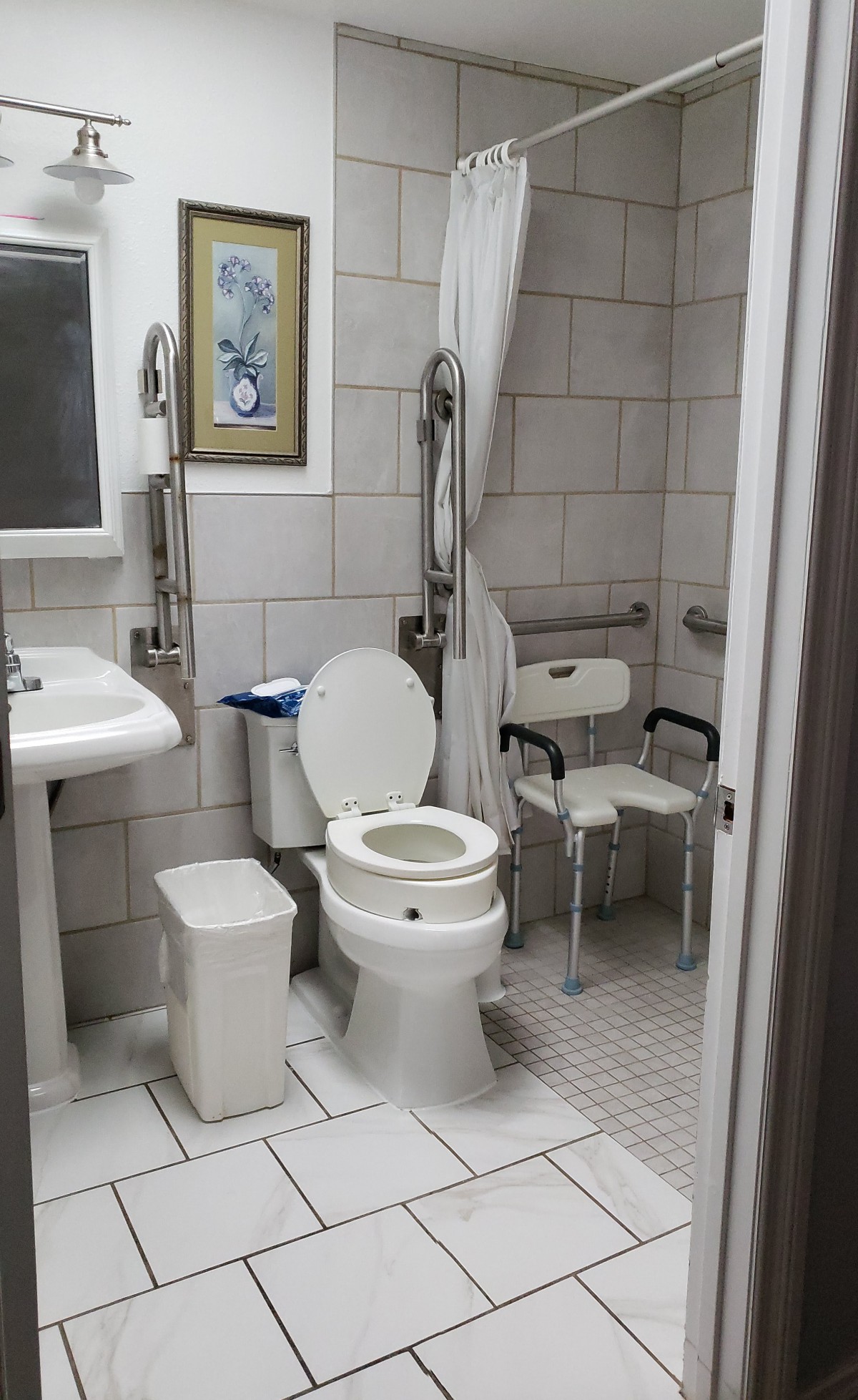 An accessible bathroom with a toilet, sink, shower chair, and grab bars.