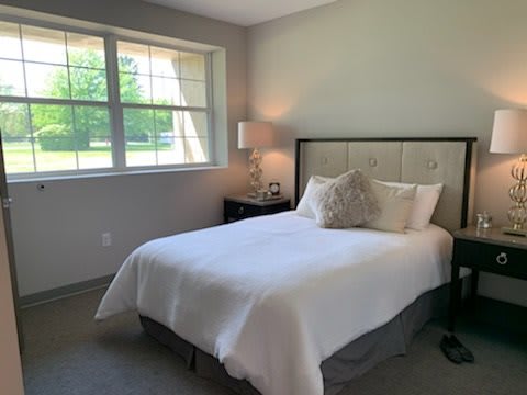 A cozy bedroom with a neatly made bed and a lamp by the window.