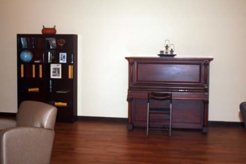 A cozy room with a wooden piano and a bookshelf against the wall.