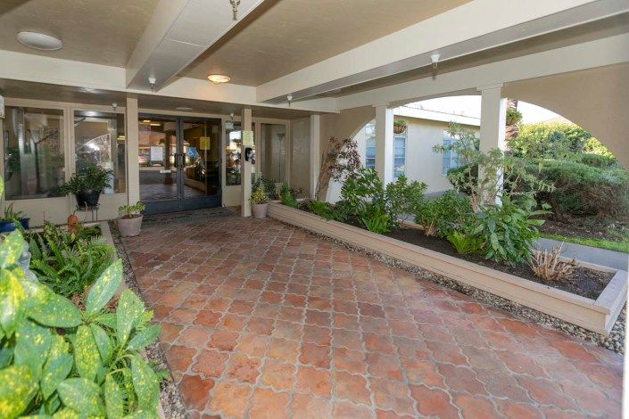 A covered entrance with terracotta pavers, surrounded by plants.