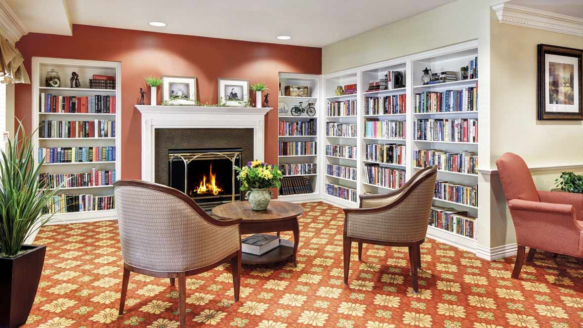 A cozy library corner with a fireplace, surrounded by bookshelves and two chairs.