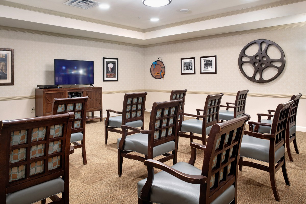 A well-arranged meeting room with chairs facing a television, surrounded by framed pictures and decor on the walls.