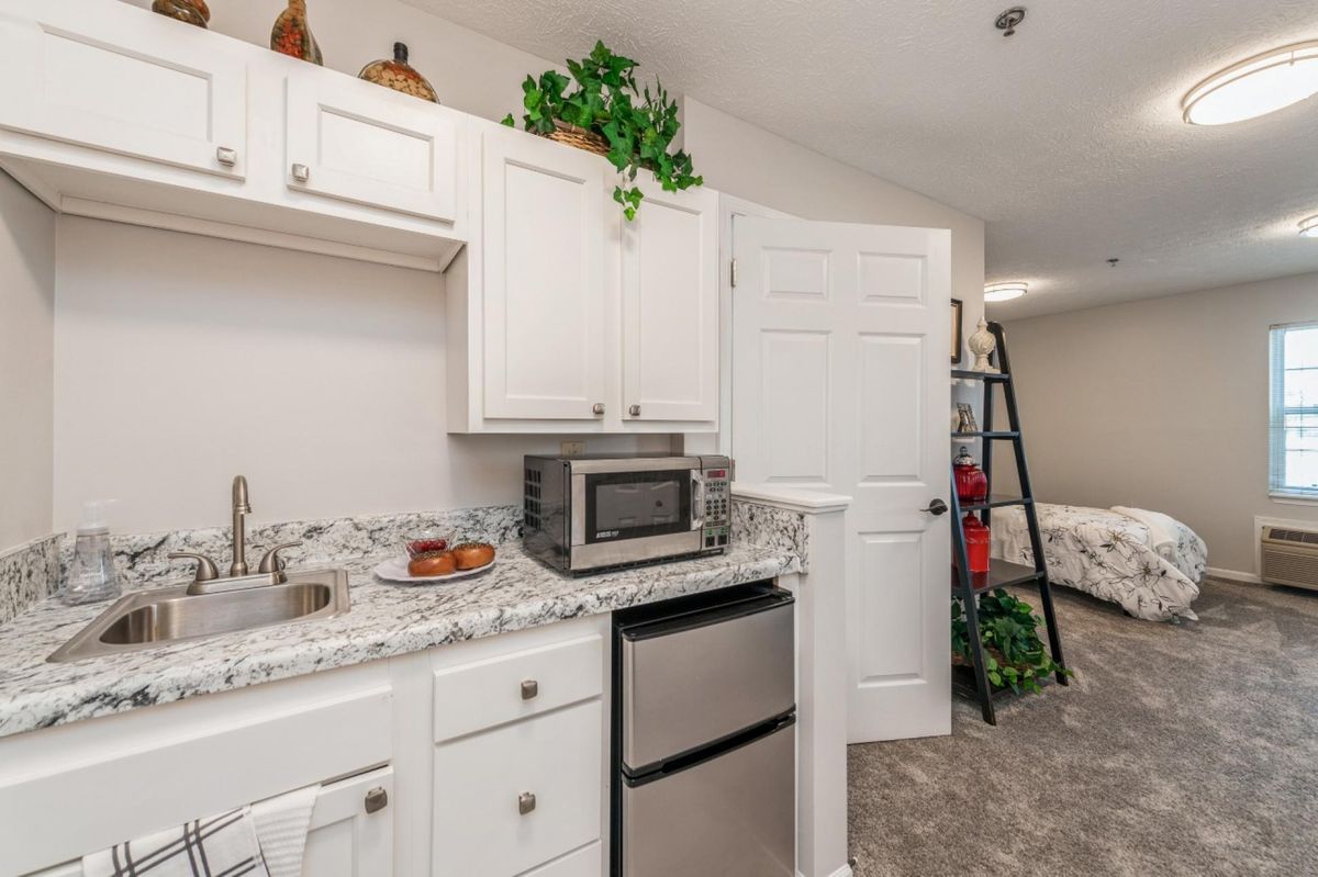 A cozy kitchen area with white cabinets, a microwave, and a mini fridge, enhanced by indoor plants and decorative items.