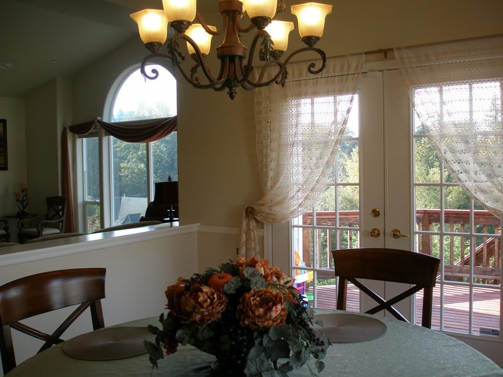A cozy dining room with a chandelier, floral centerpiece, and large windows.