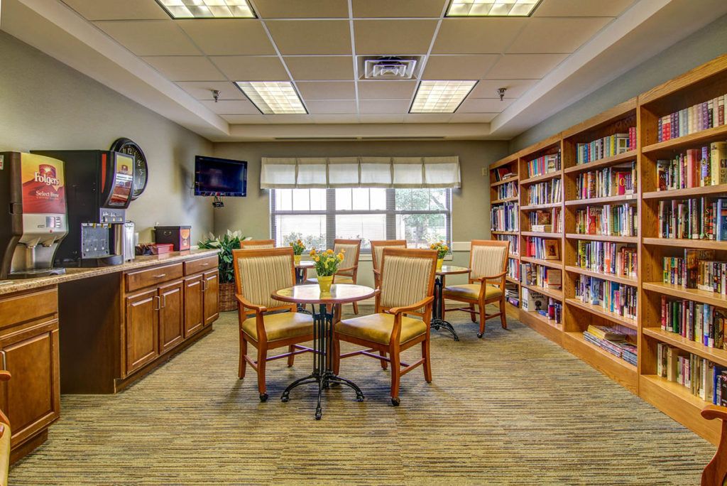 A cozy library reading area with bookshelves, tables, and chairs.