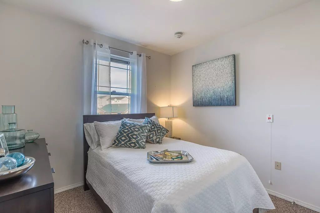 A cozy bedroom with a neatly made bed, soft lighting, and calming artwork on the wall.