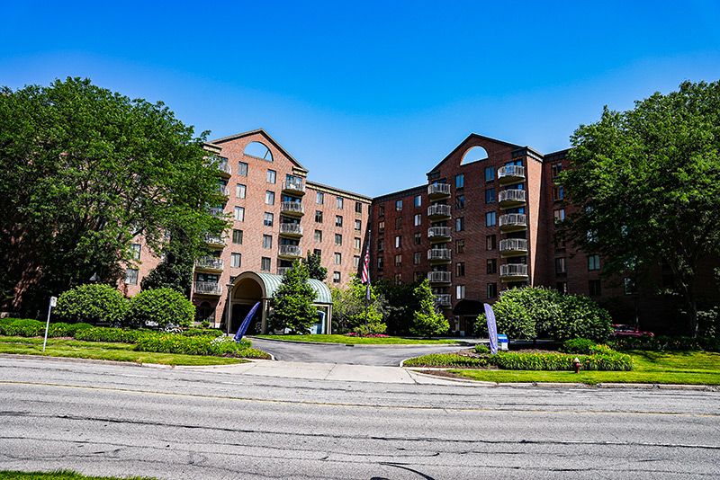 A large brick apartment building surrounded by greenery under a clear blue sky.