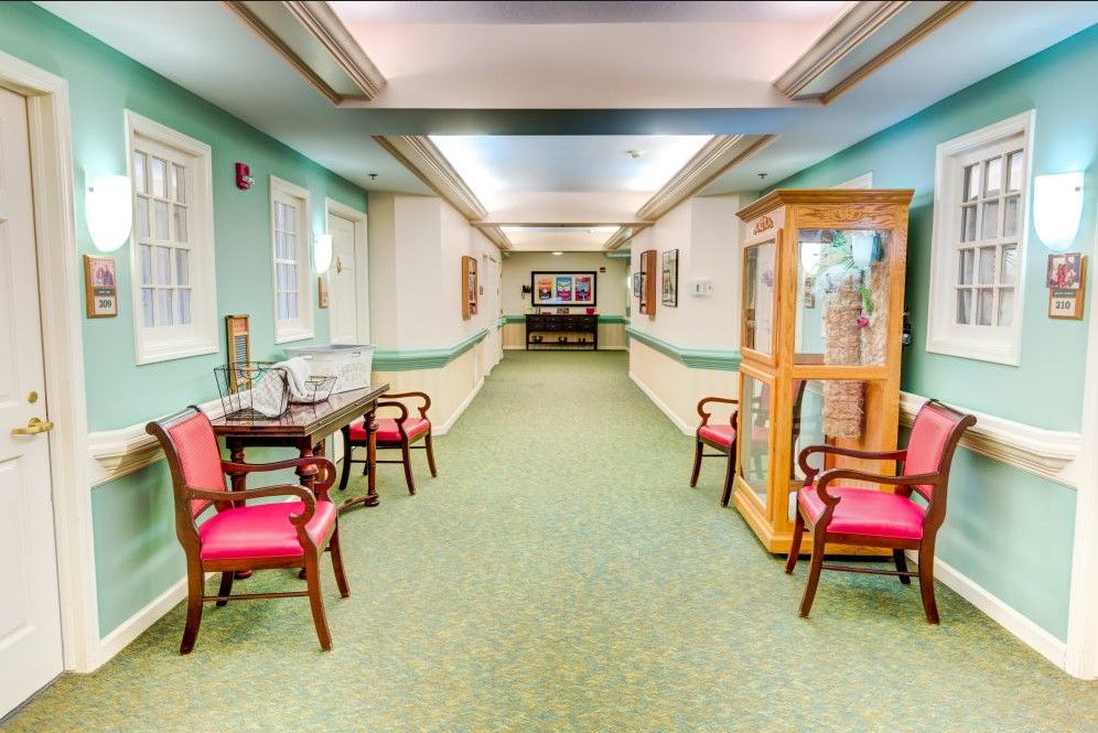 A well-lit hallway with green carpet and red cushioned chairs, featuring a wooden display case.