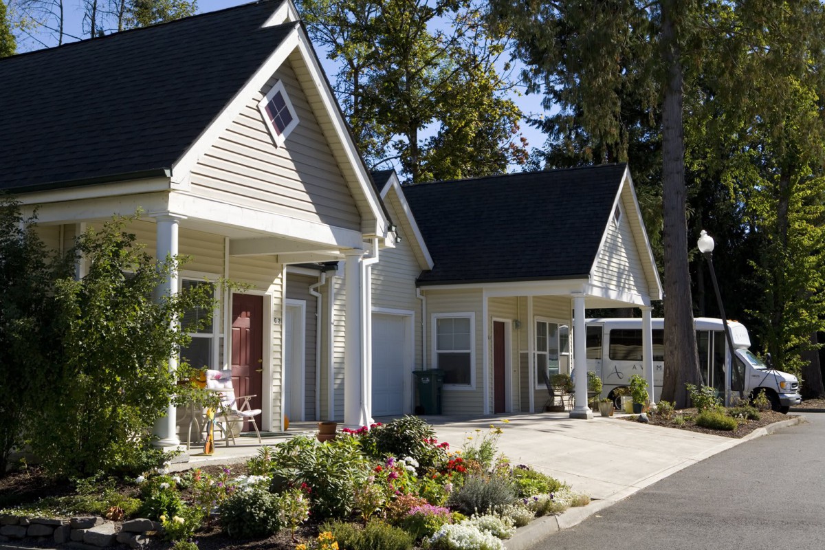 A charming cottage-style house with a beautifully landscaped garden and driveway, surrounded by trees.