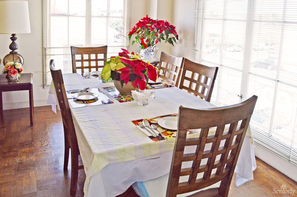 A dining table set with a white tablecloth and decorated with poinsettia flowers.