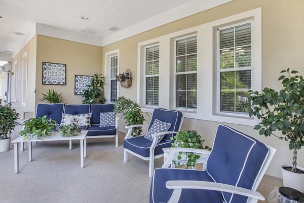 A cozy patio seating area with blue cushioned chairs, decorated with plants and artwork.