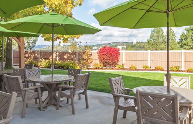 A serene outdoor patio with green umbrellas and seating, surrounded by a lush garden.