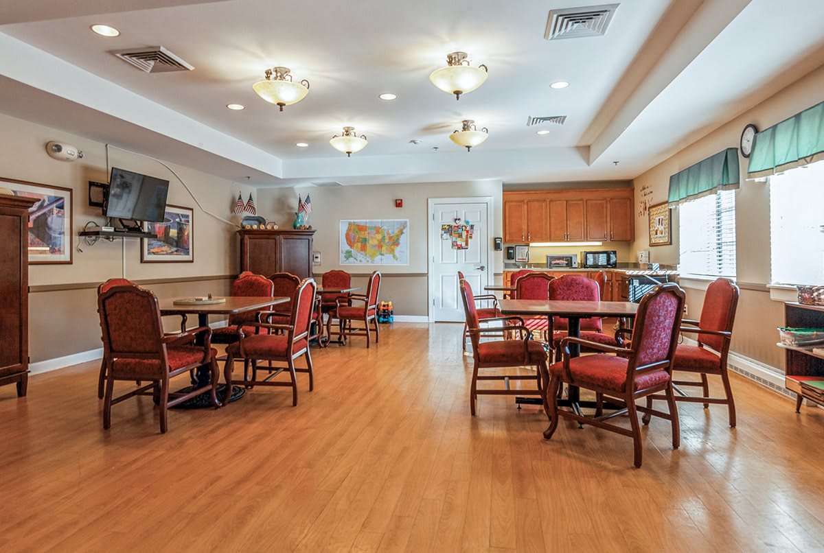 A spacious dining room with multiple tables and chairs, featuring a kitchen area in the background.
