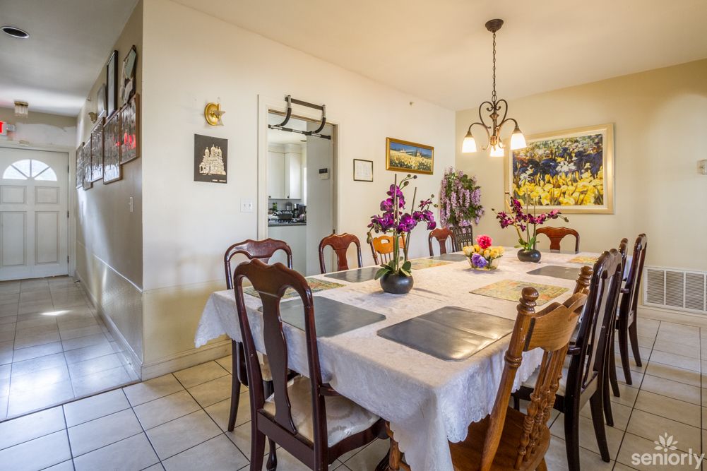 A well-decorated dining room with a table set with flowers and placemats under a chandelier.