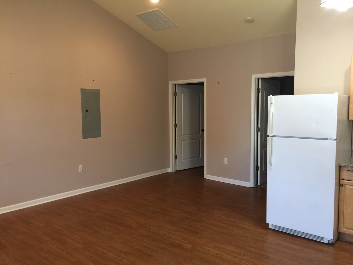An empty apartment interior featuring hardwood floors, a white refrigerator, and two doors.
