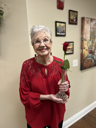 A joyful elderly woman holds a single red rose in a cozy indoor environment.