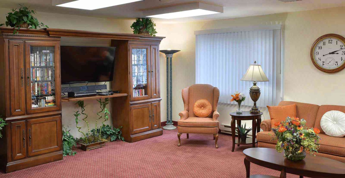 A cozy living room with an armchair, wooden bookshelf, and a television.