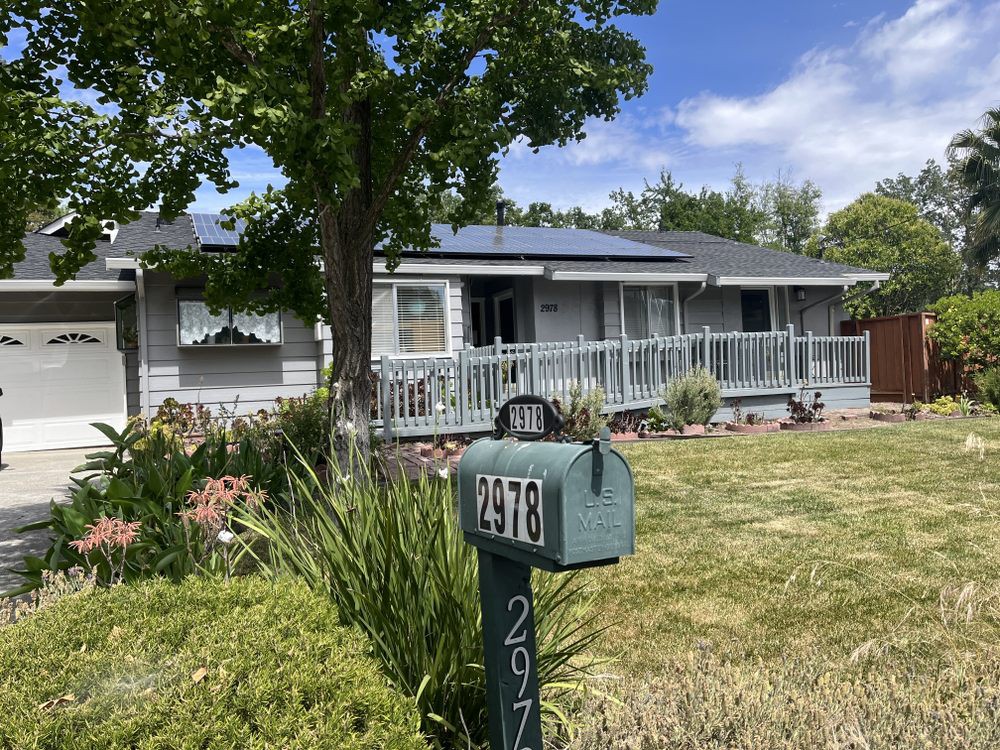 A suburban house with solar panels and a mailbox in the front yard on a sunny day.