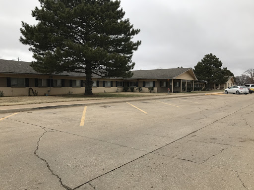 A spacious commercial building with an empty parking lot, framed by trees under a cloudy sky.
