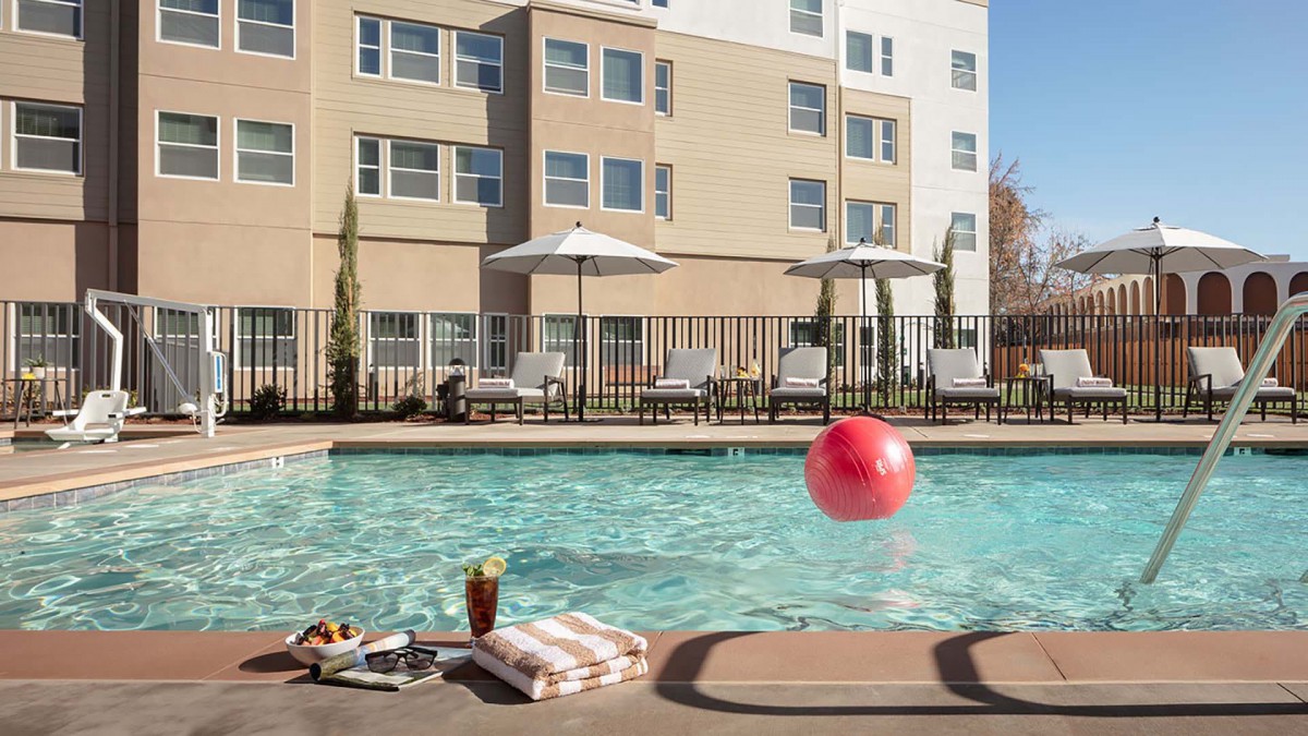 A relaxing hotel swimming pool area with sun chairs and a vibrant red beach ball.