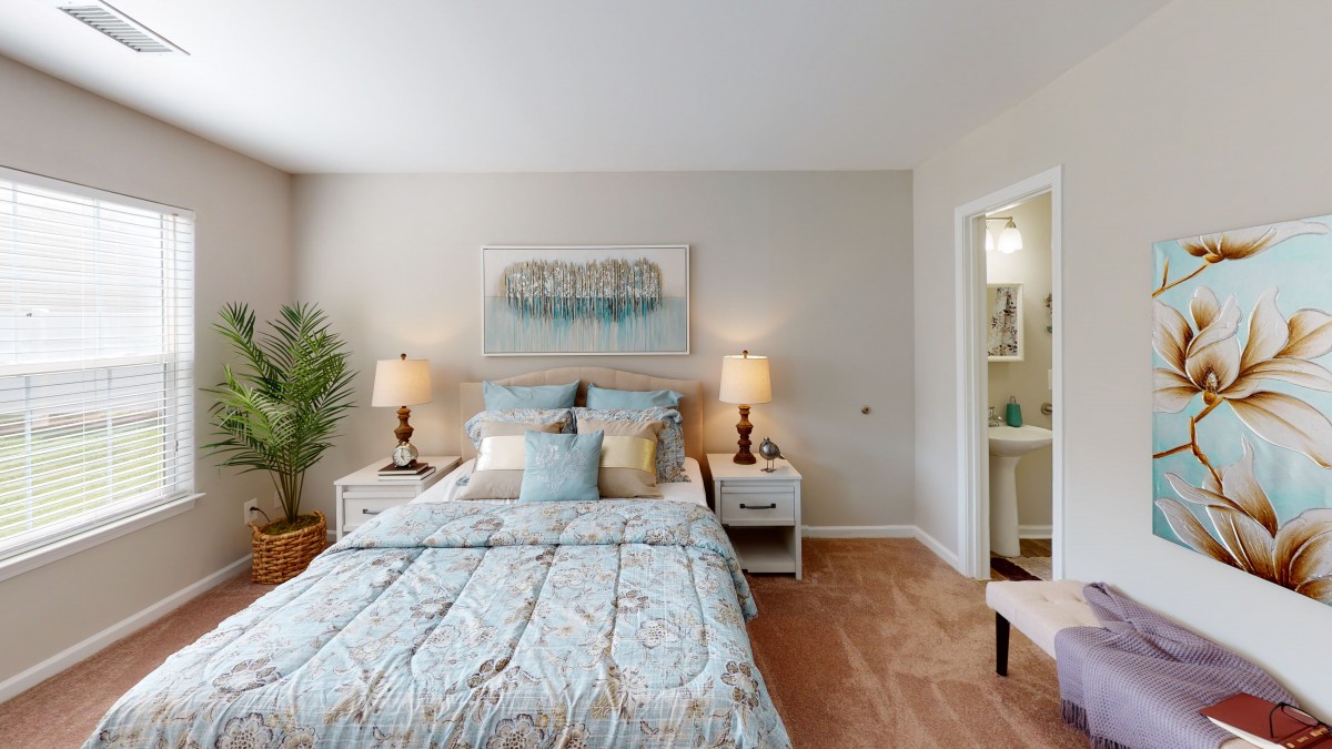 A cozy and elegantly decorated bedroom with a comfortable bed, nightstands, lamps, artwork, and a touch of greenery.