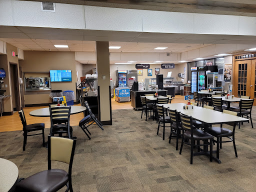 A spacious dining area featuring several tables and chairs, along with vending machines in the background.