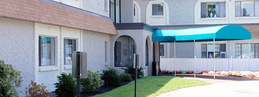 An exterior view of a building featuring arched windows, a green awning, and well-maintained landscaping.