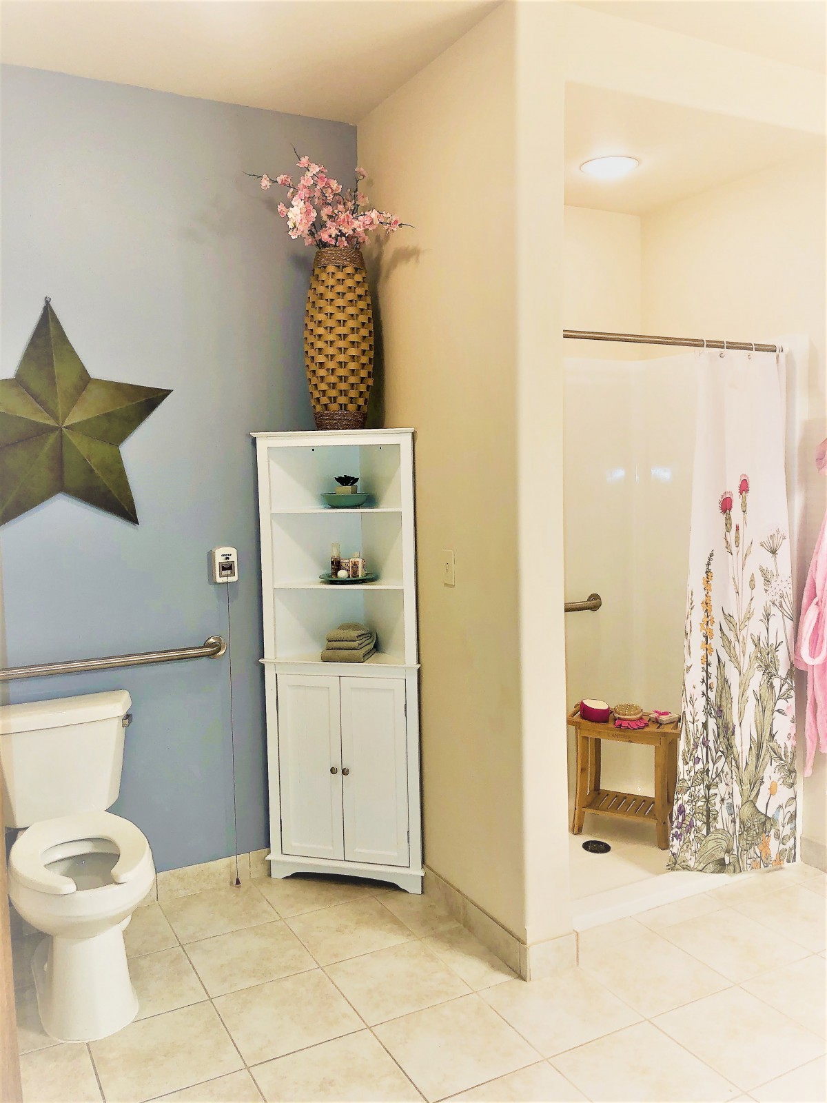 A bathroom featuring a star wall decor, white storage cabinet with pink flowers, and a shower area with a patterned curtain.