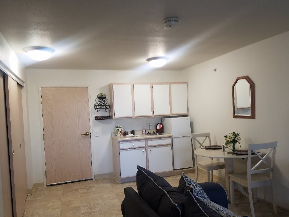 A small apartment kitchen with white cabinets, a table with chairs, and some appliances.