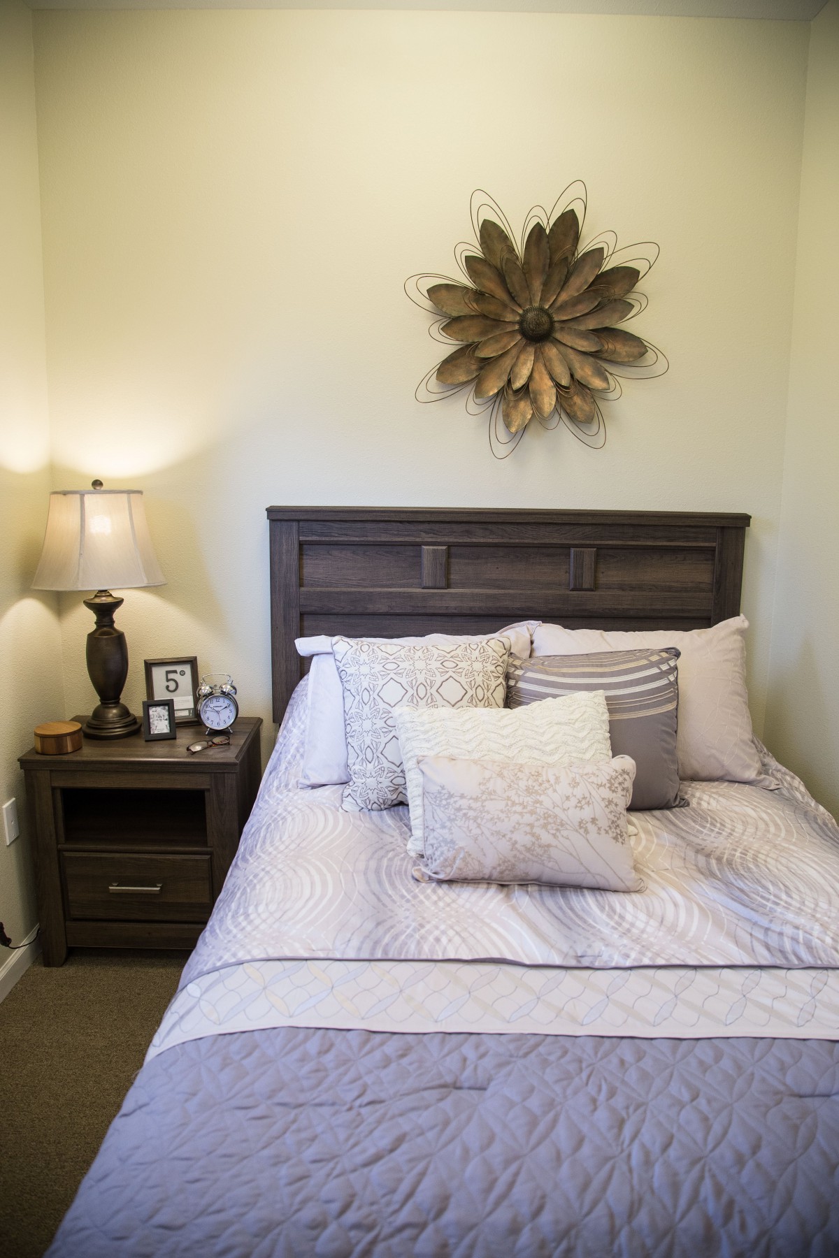 A cozy bedroom with decorative pillows, a bedside lamp, and wall art above the headboard.