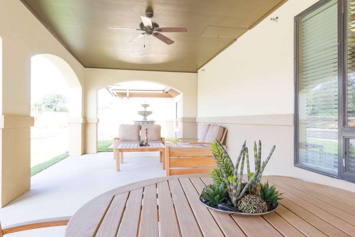 A modern outdoor patio featuring comfortable seating, a ceiling fan, and decorative plants.