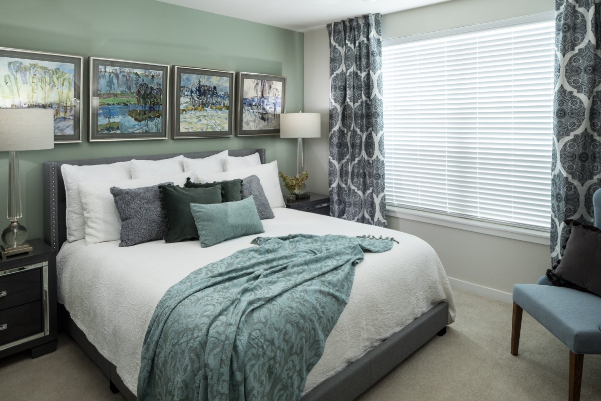 A modern bedroom featuring a neatly made bed with green accents, decorative pillows, and elegant wall art.