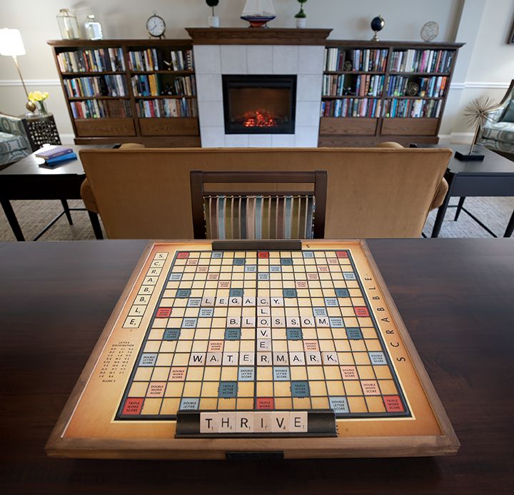 A cozy library setting with a Scrabble board ready for play in front of a fireplace and bookshelves.